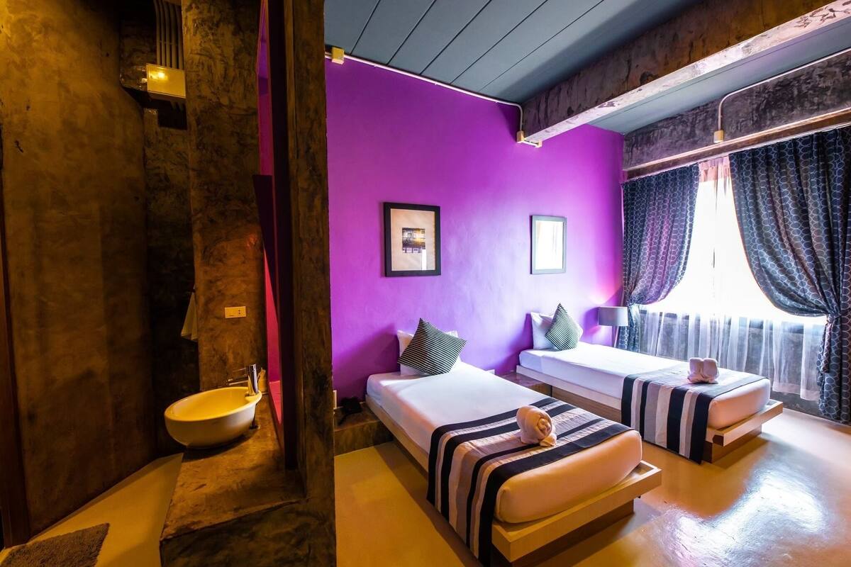 A room with two beds, a sink, and a purple wall.