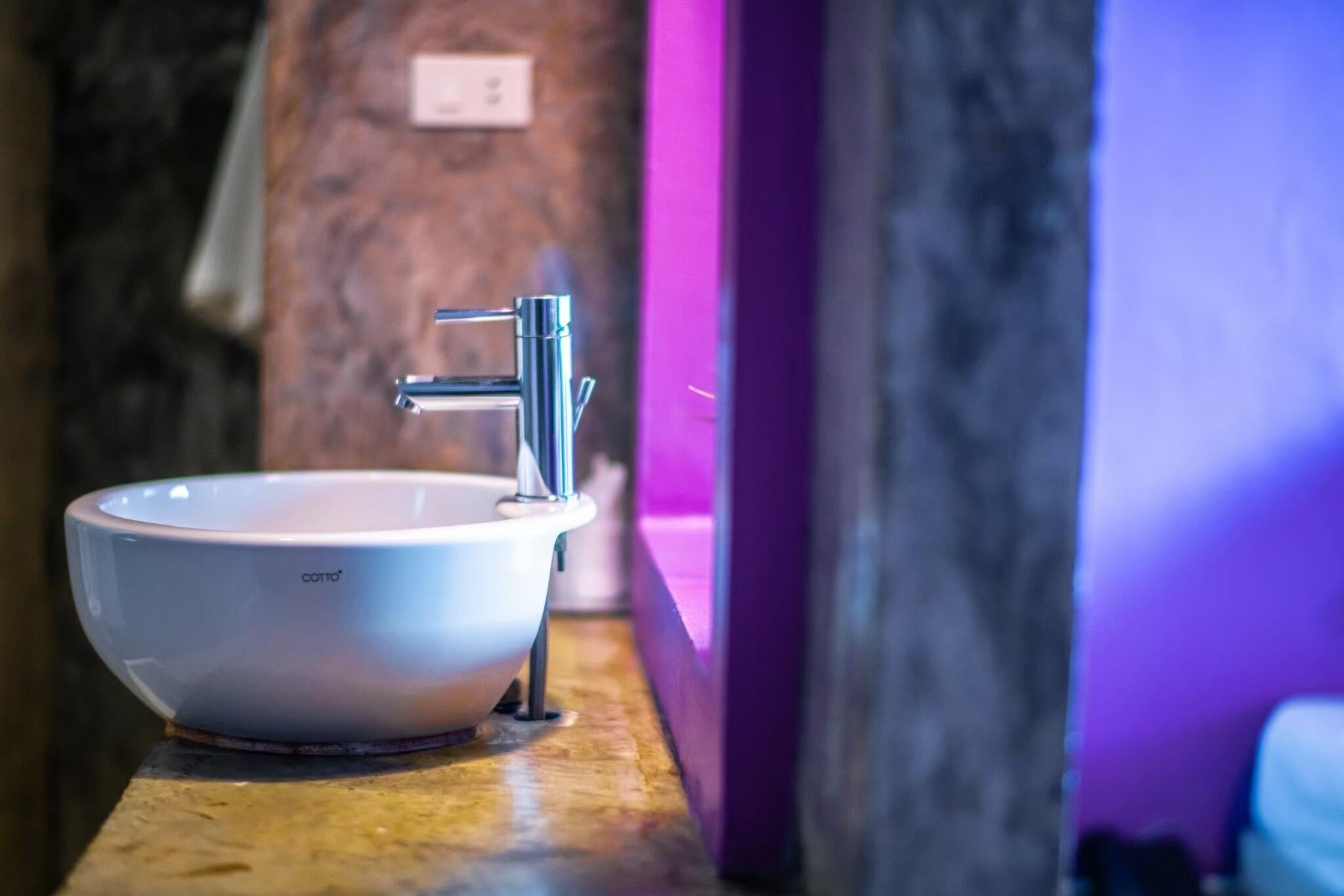 Uma pia de cerâmica branca com uma torneira moderna sobre uma bancada de mármore em um banheiro.