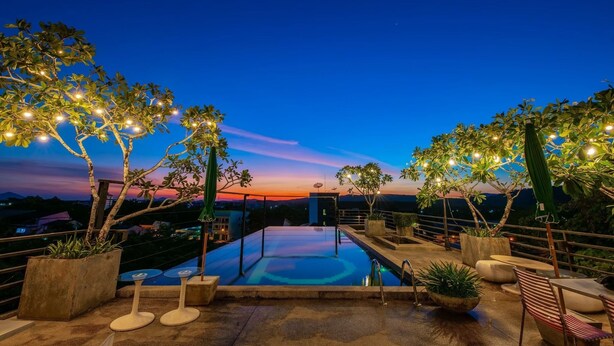 Zona de piscina en la azotea con vistas a la puesta de sol, rodeada de plantas en macetas y mobiliario de exterior.