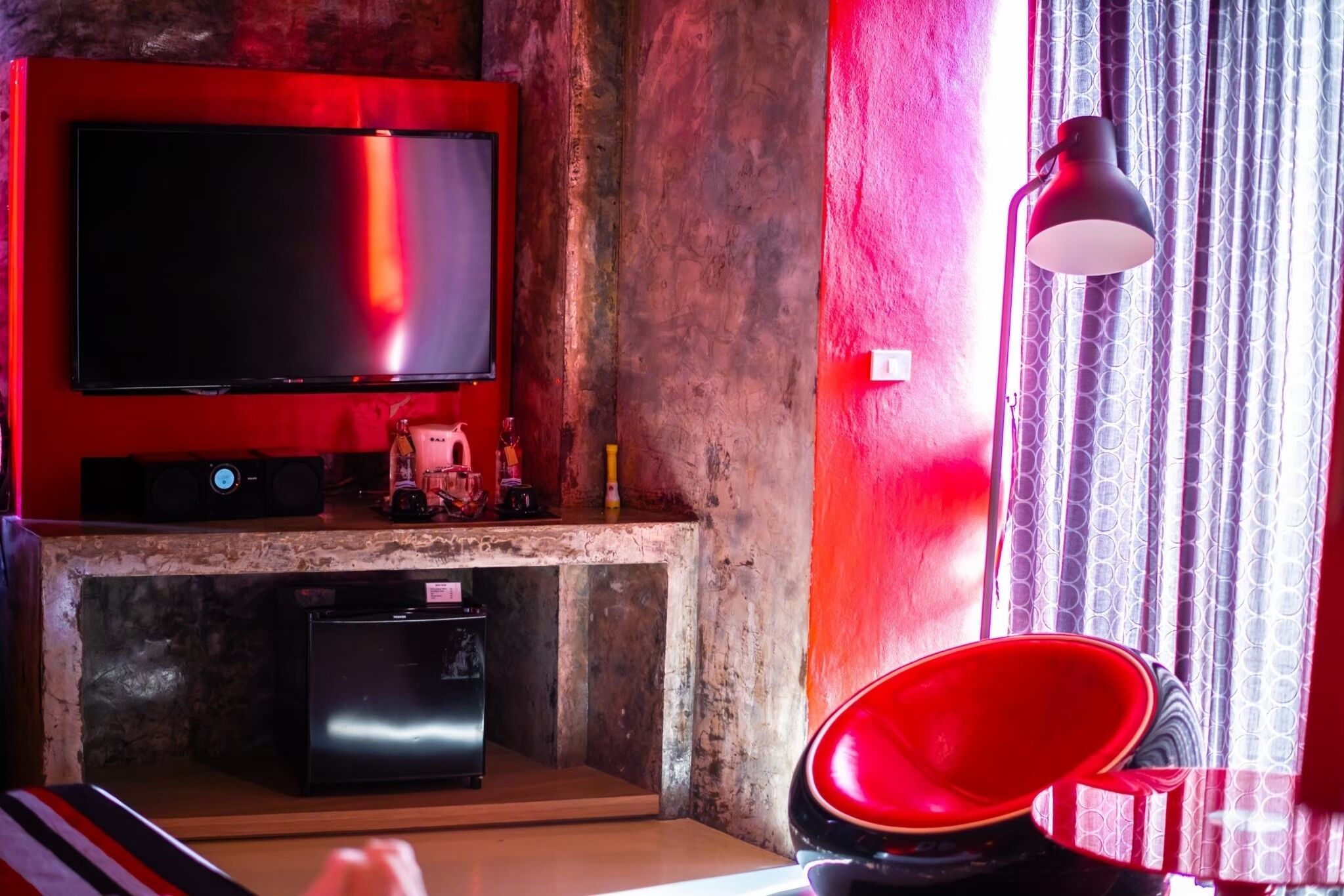 A living room with a flat-screen TV mounted on a red wall, a small black speaker, and a red chair.