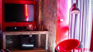 A living room with a flat-screen TV mounted on a red wall, a small black speaker, and a red chair.