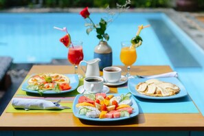 Una mesa con alimentos para el desayuno, incluyendo una bandeja de frutas, una porción de panqueques, una jarra de café y dos bebidas.