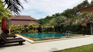 A rectangular swimming pool with a metal ladder, surrounded by lush greenery and a building with a red roof. - Palm Sweet Resort (Chumphon)