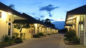 A row of motel buildings with a paved walkway between them, each with a door and a small porch area. - Palm Sweet Resort (Chumphon)