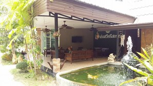 A covered outdoor seating area with a pool, wooden furniture, and a fountain. - Palm Sweet Resort (Chumphon)