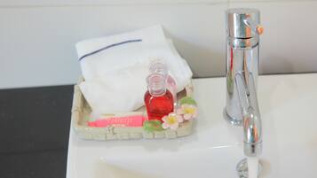 Et badeværelsesvask med hane, sæbedispenser og en lille bakke med shampoo og sæbe.