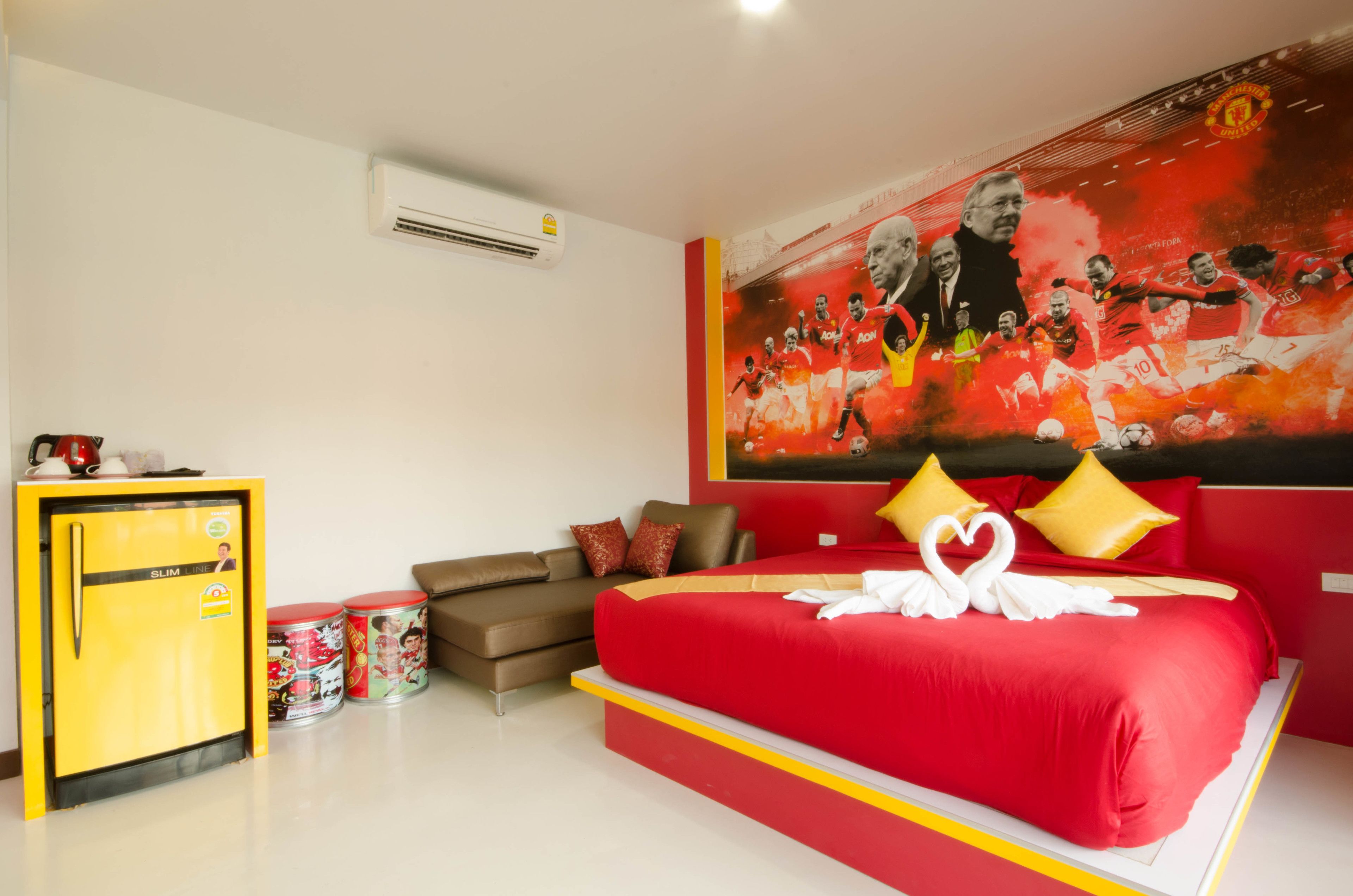 A hotel room with a large bed, a sofa, a small yellow refrigerator, and a wall mural.
