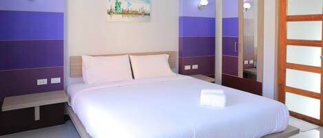 A neatly made bed in a hotel room with a large mirror and a painting of the Statue of Liberty on the wall.
