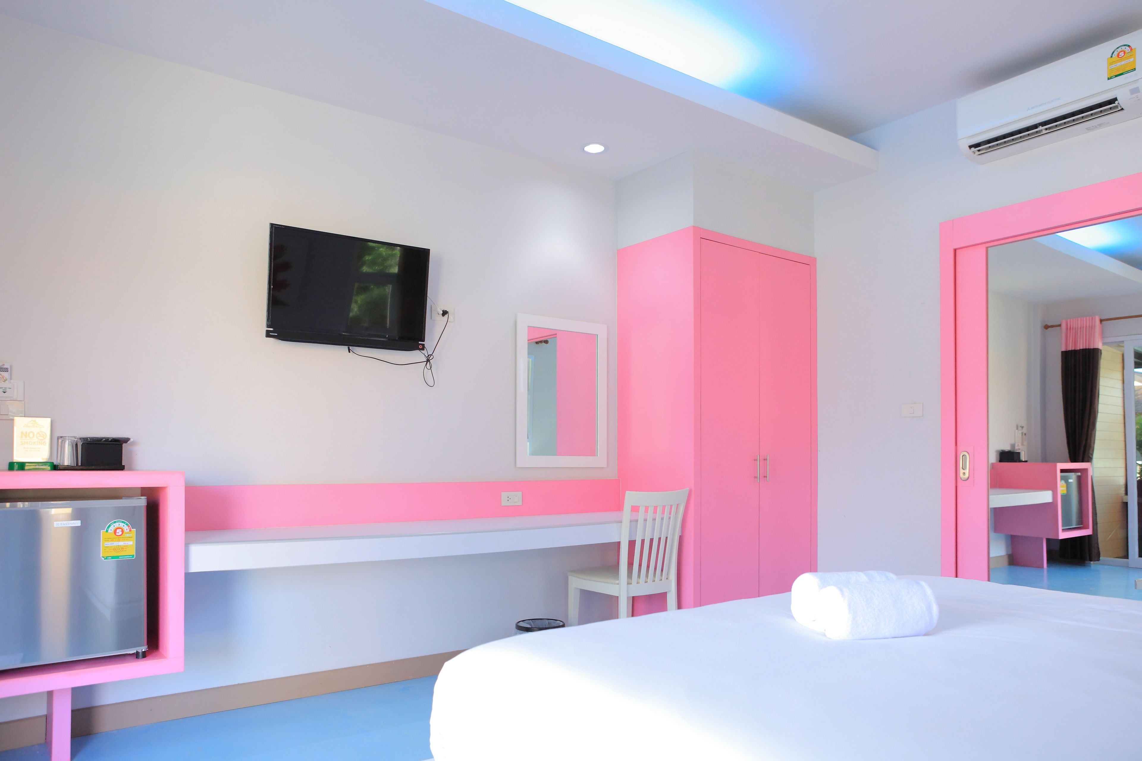 Een hotelkamer met een bed, een bureau, een stoel, een televisie en een roze garderobe.