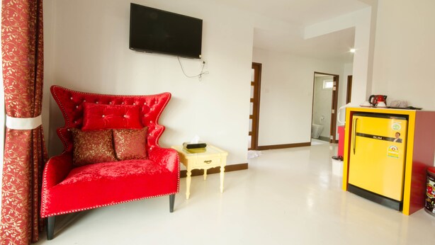 A room with a red velvet sofa, a small table with a tissue box, a yellow refrigerator, and a flat-screen TV mounted on the wall. - Pueanjai Resort and Restuarant (Chumphon)