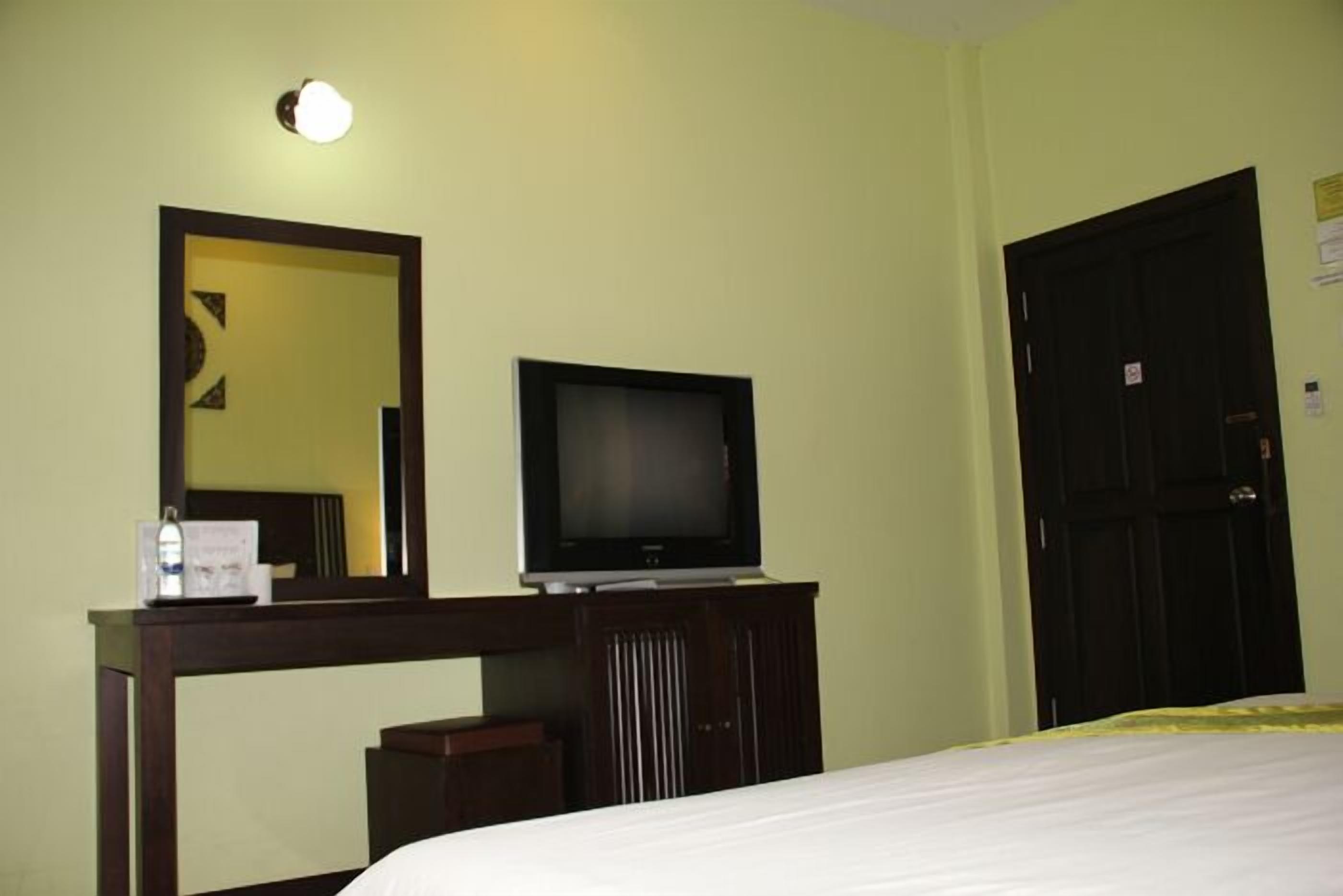 Habitación de hotel con una cama, un televisor sobre un soporte de madera, un espejo y una puerta.