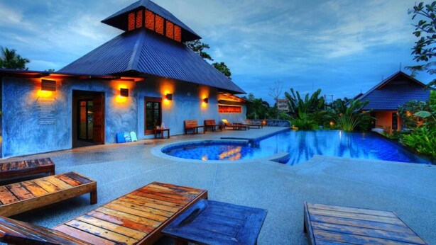 A resort with a swimming pool, wooden lounge chairs, and a building with a sloped roof.