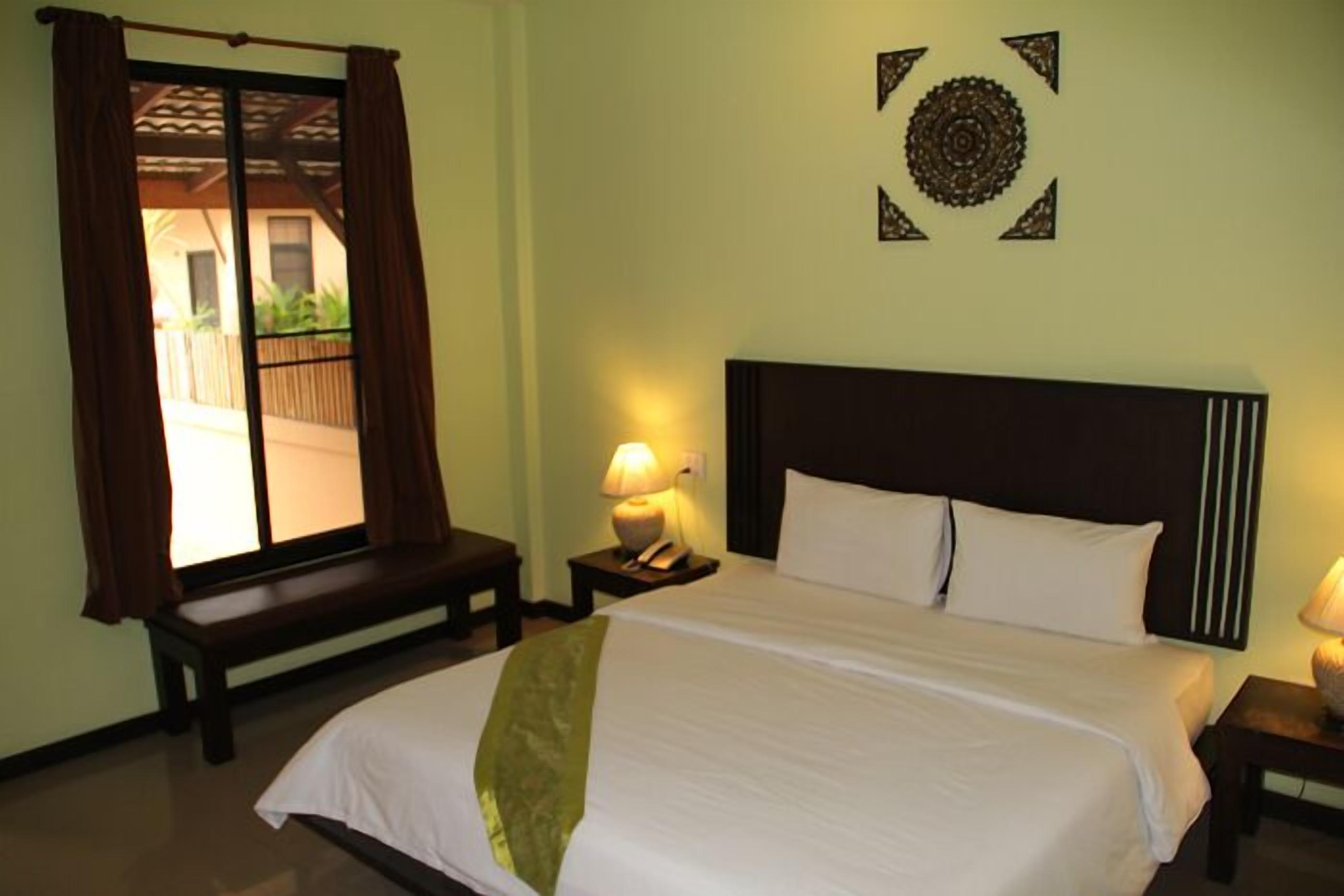 Habitación de hotel con cama, un banco, una mesita de noche con lámpara y vistas al exterior.