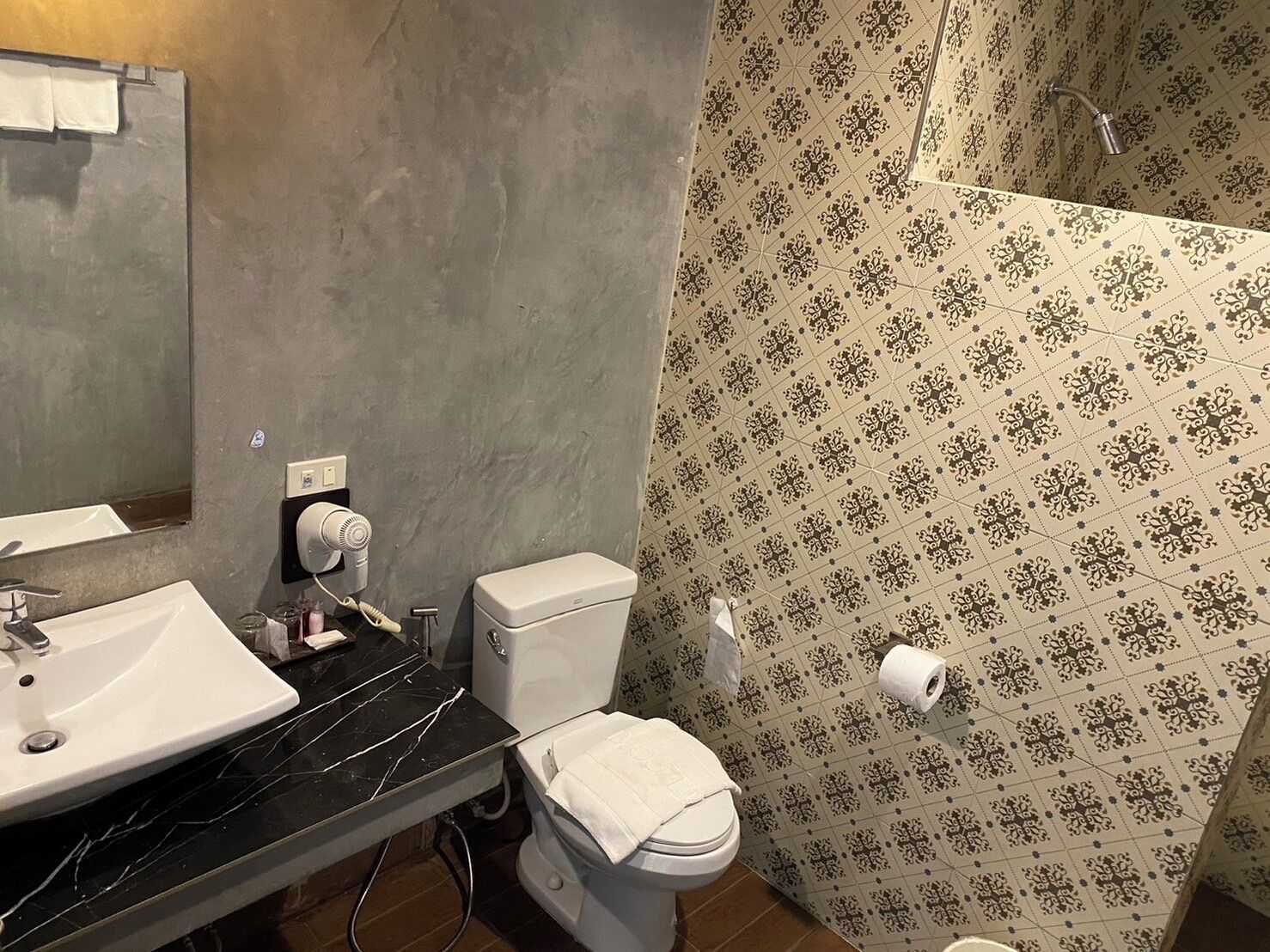 A bathroom with a white toilet, a sink with a black countertop, and a shower area with patterned tiles.