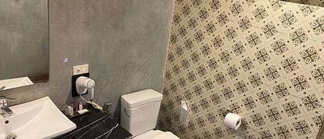 A bathroom with a white toilet, a sink with a black countertop, and a shower area with patterned tiles.