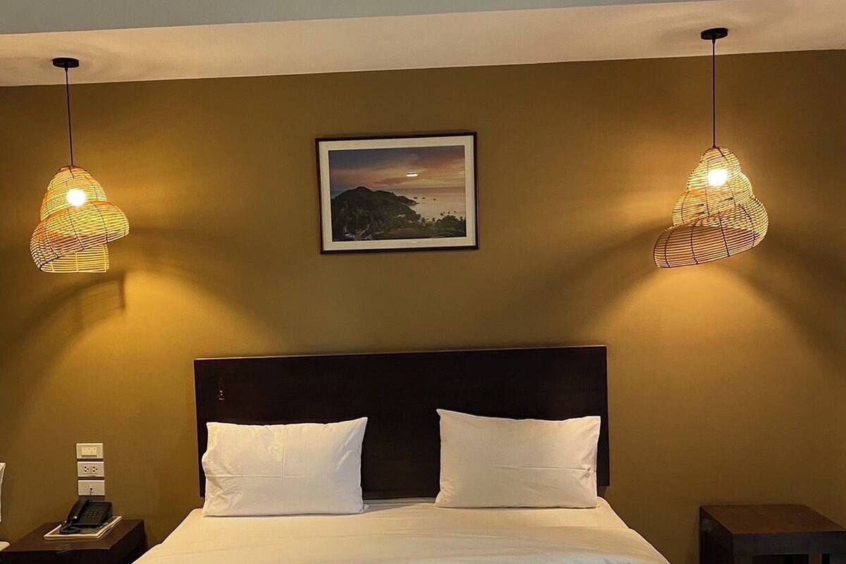 A hotel room with a large bed, two bedside tables, a nightstand, and two hanging lamps.