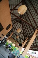 Un espacio al aire libre techado con un techo alto, vigas metálicas y lámparas colgantes.