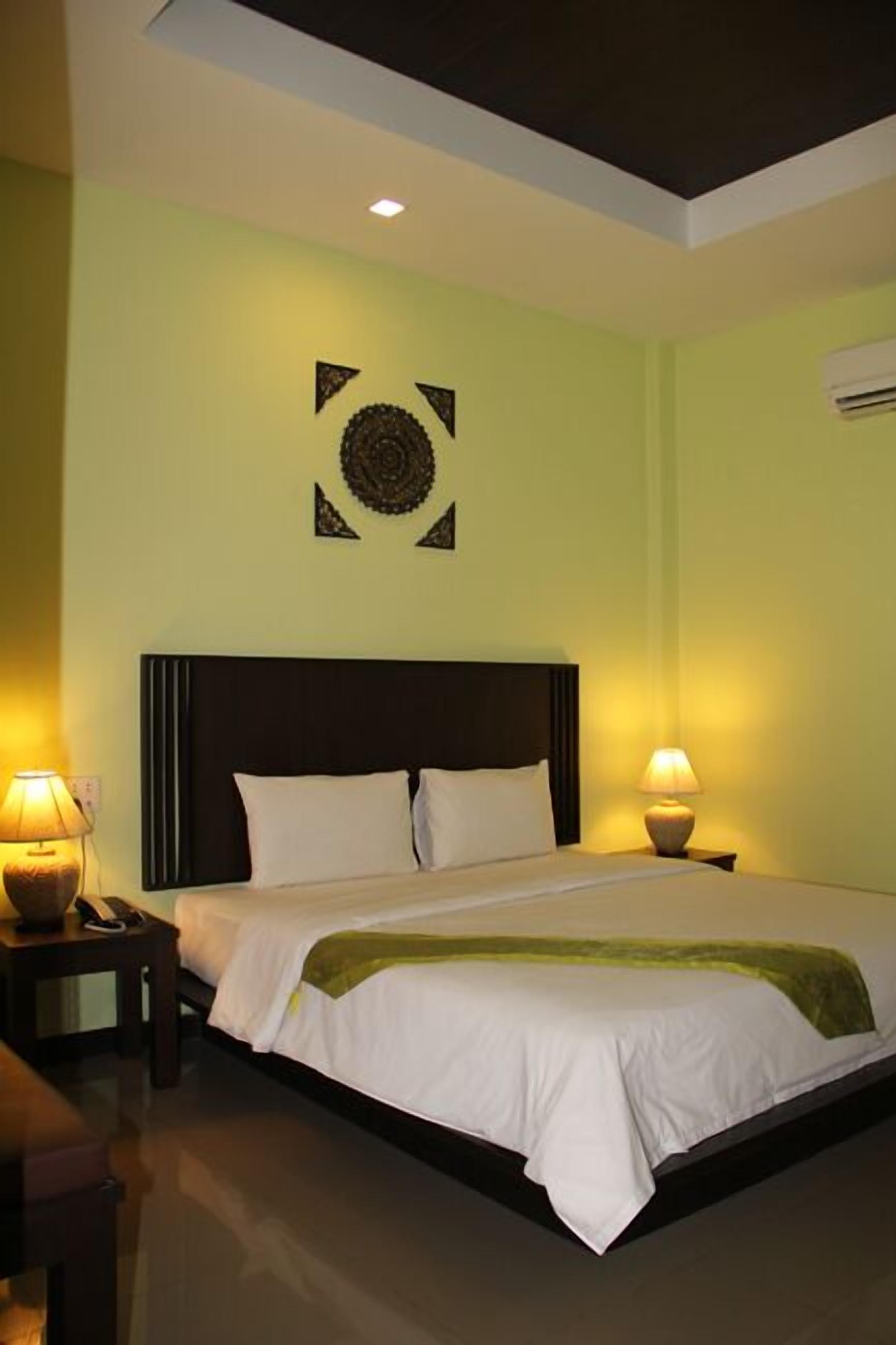 A hotel room with a bed, two bedside lamps, a wall decoration, and an air conditioning unit.
