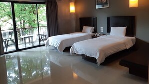 A hotel room with two beds, a large window with a view of greenery, and a balcony.