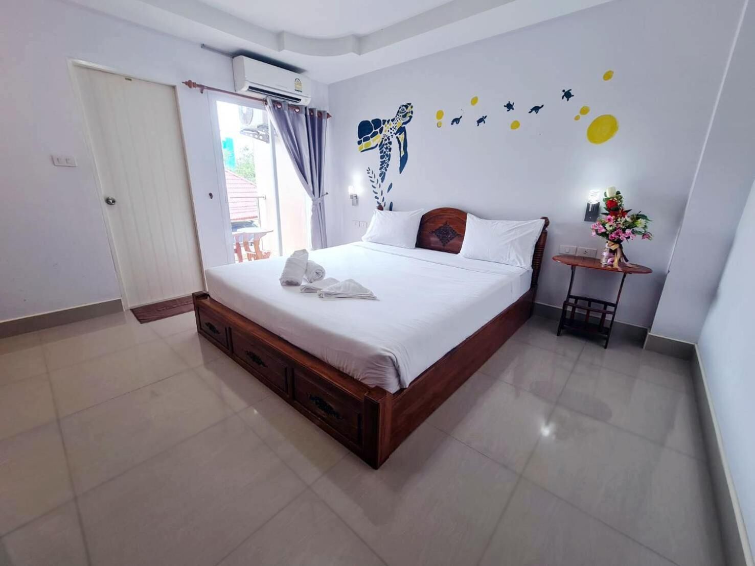 A hotel room with a bed, a small table with a vase, and a wall decoration.