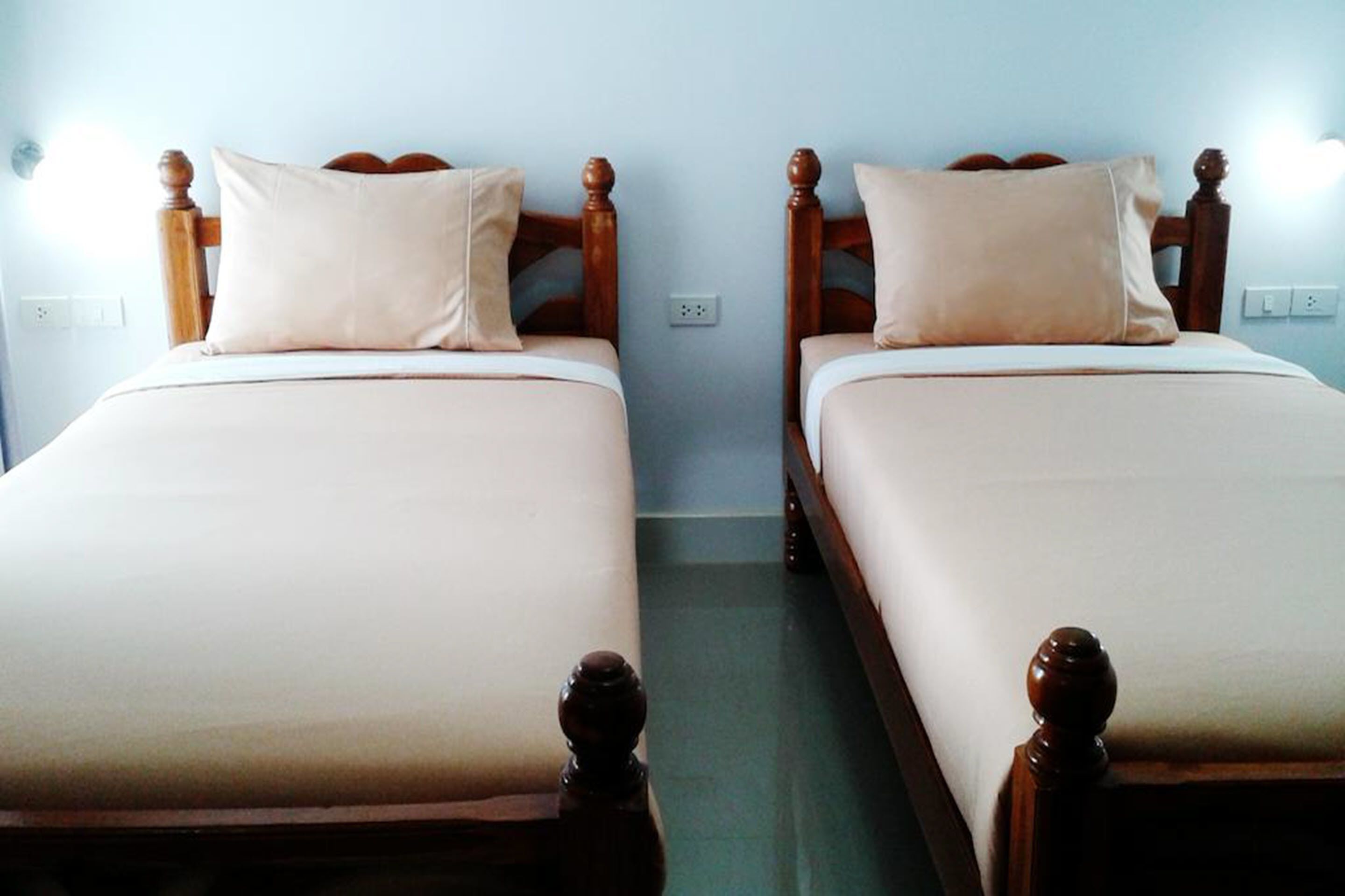 Two single beds with wooden headboards and beige bedding in a room with light blue walls.