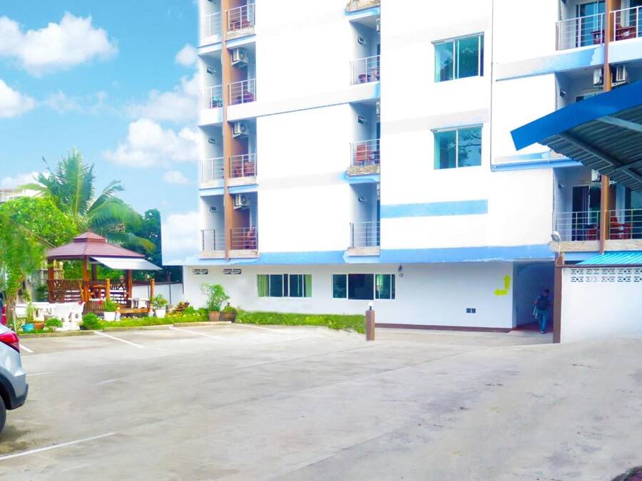 A multi-story hotel with a parking area, a covered entrance, and a small outdoor seating area.
