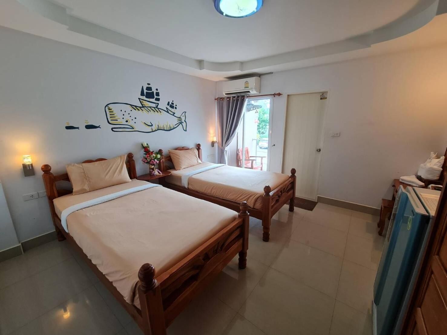 Habitación de hotel con dos camas de madera, un mural de peces en la pared, una lámpara de techo y una puerta corrediza de cristal al exterior.