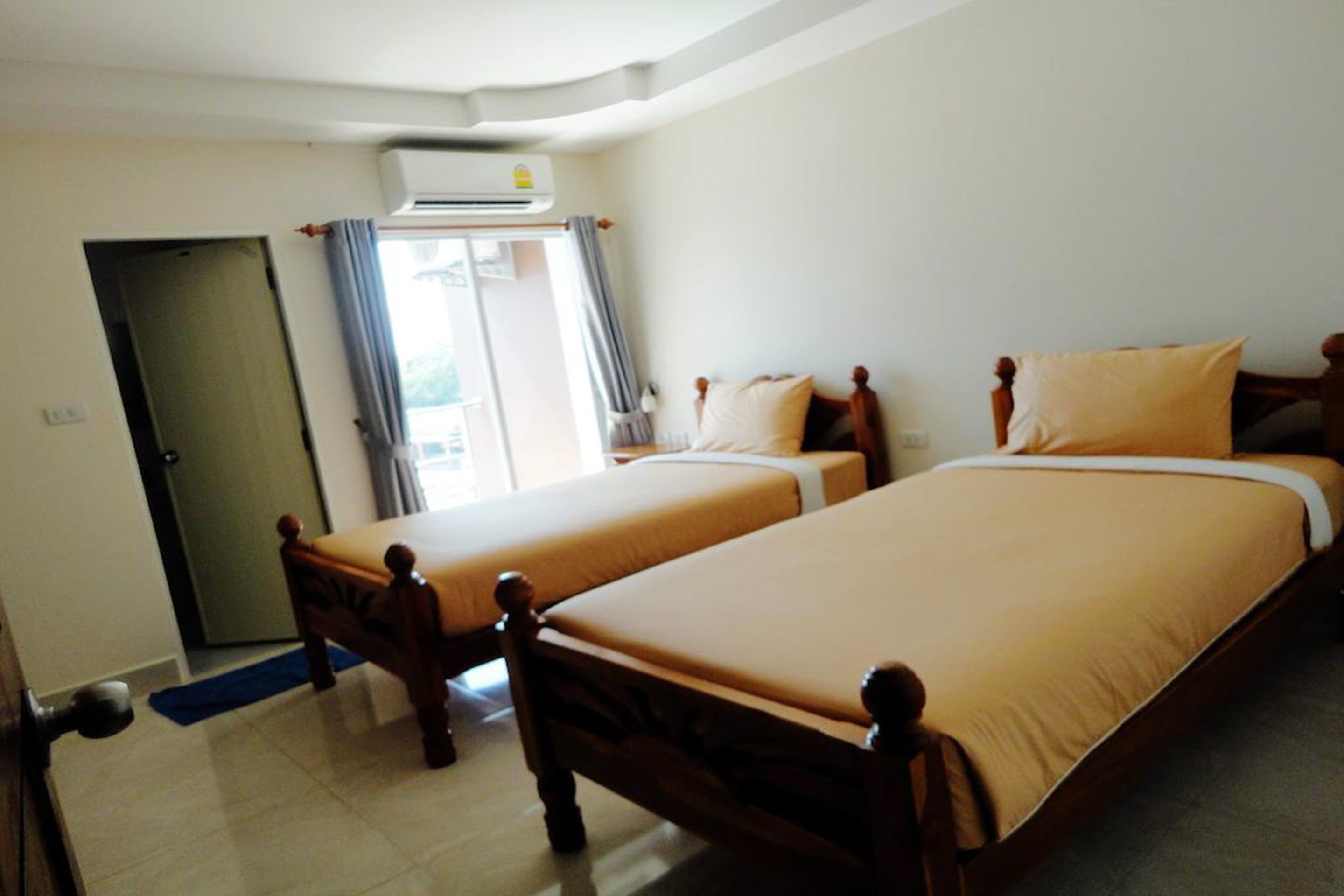 A hotel room with two single beds, a door, an air conditioning unit, and a view of the outside.