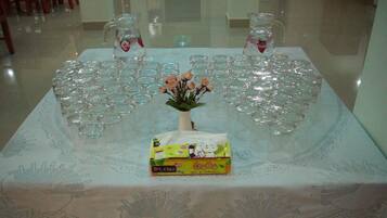 A table with a lace tablecloth, two pitchers, a vase with flowers, and a box of tissues.