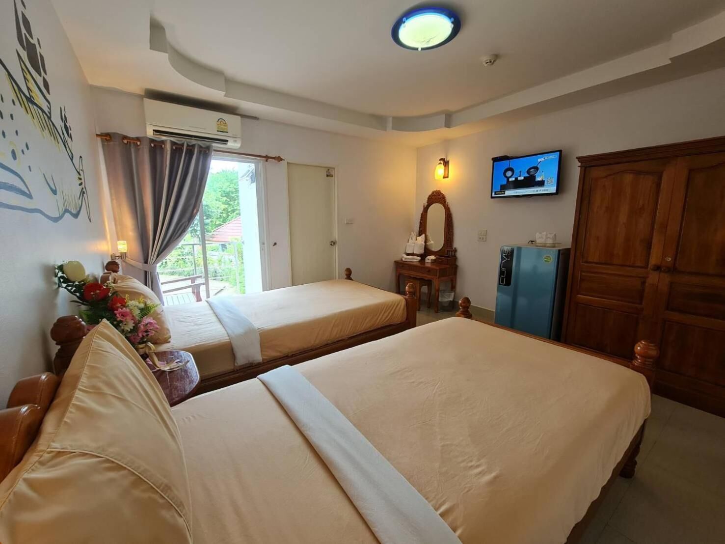 A hotel room with two beds, a television, an air conditioning unit, a wooden wardrobe, and a window with curtains.