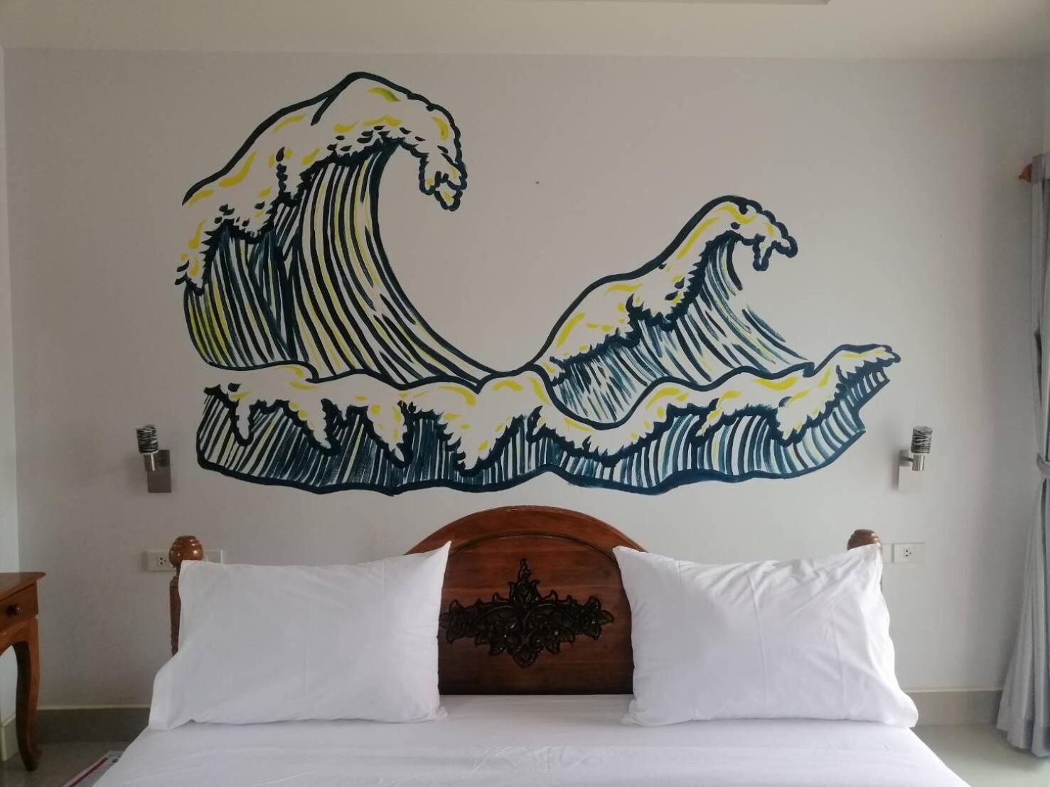 Habitación de hotel con un cuadro grande de una ola en la pared, cabecera de madera y ropa de cama blanca.