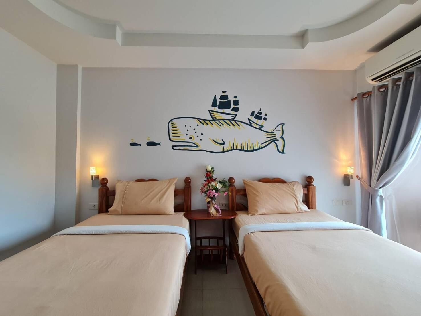 Habitación de hotel con dos camas, un mural de un pez y una mesita con un jarrón de flores.