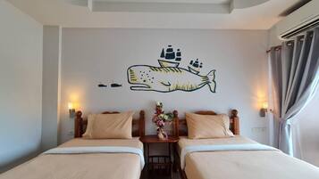 Habitación de hotel con dos camas, un mural de un pez y una mesita con un jarrón de flores.