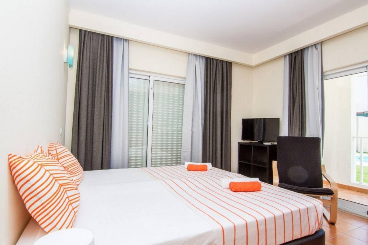 A hotel room with a bed, a TV, a chair, and a window with curtains.
