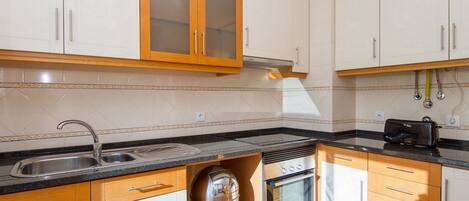 A modern kitchen with white cabinets, a stainless steel sink, and a built-in oven.
