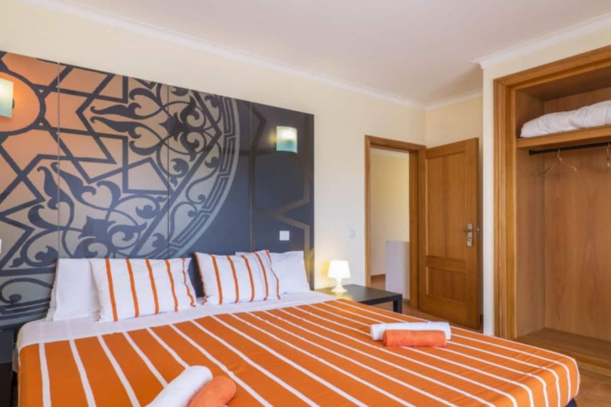 A hotel room with a large bed, a wooden wardrobe, and a decorative wall piece.