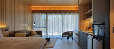 A modern hotel room with a large bed, a desk, and a kitchenette.