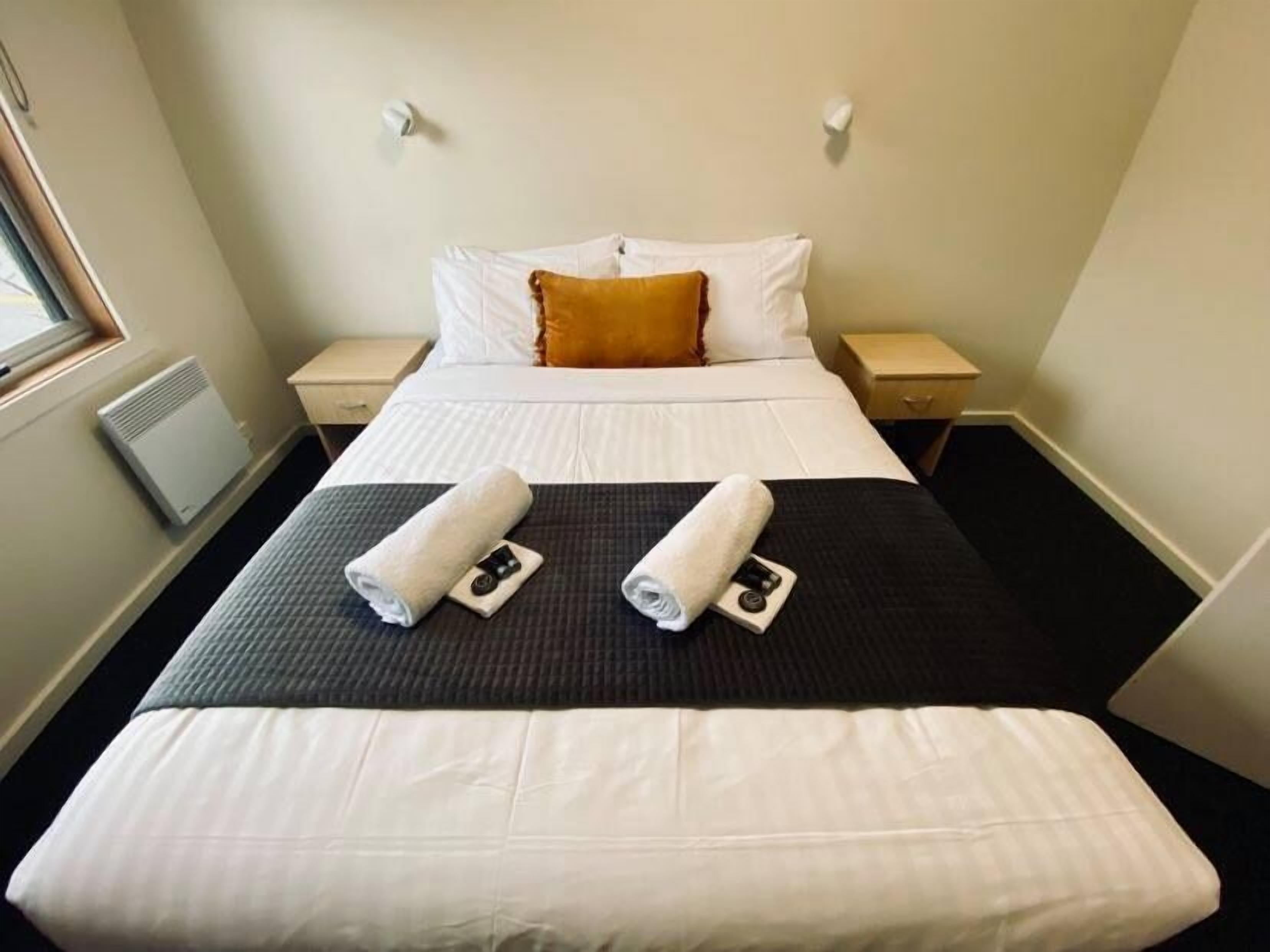 A neatly made bed with white and black bedding, two rolled towels, and a single pillow.