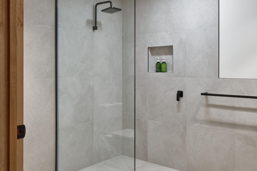 A modern bathroom with a glass shower enclosure, a small shelf with toiletries, and a towel rack.