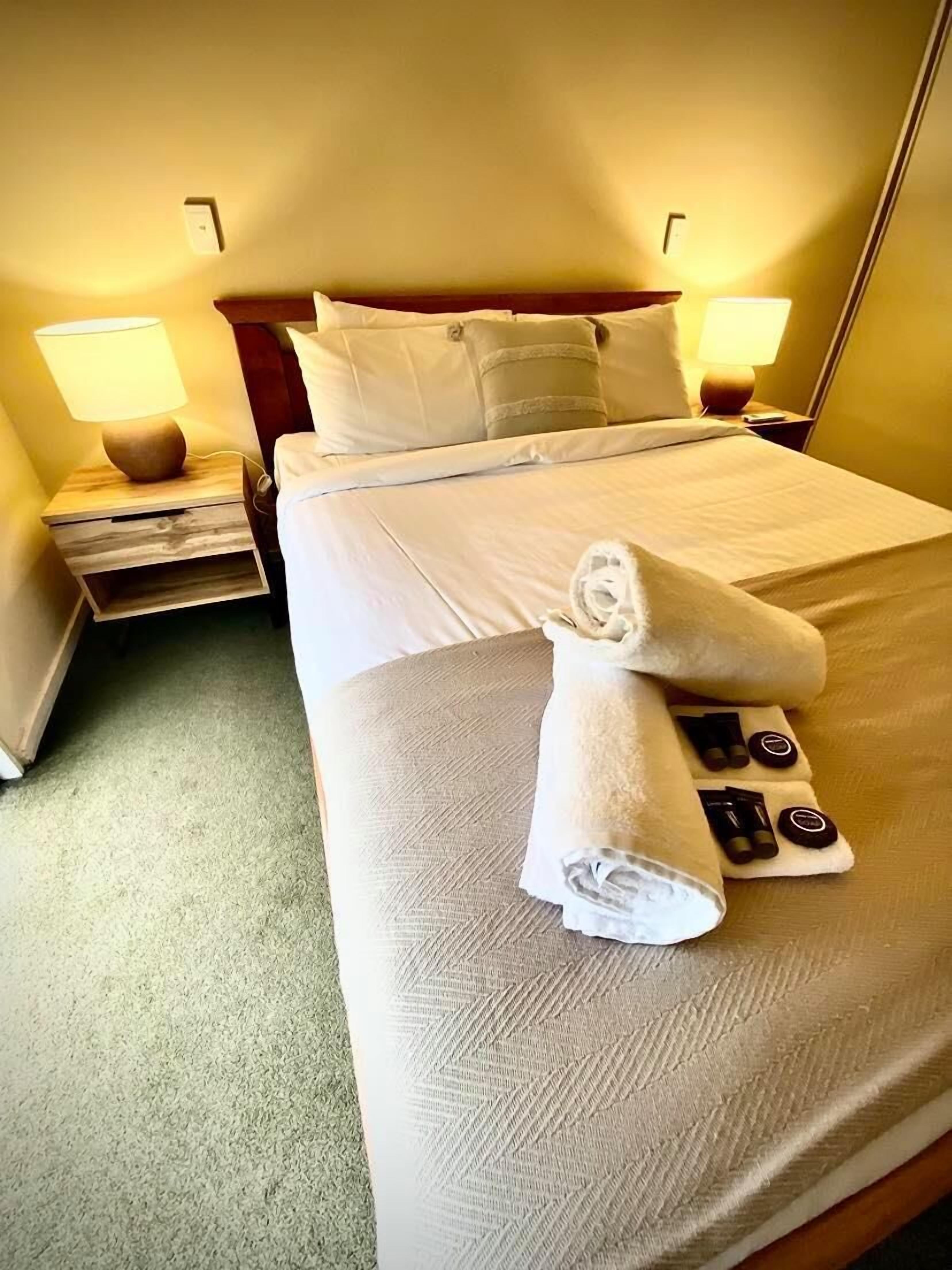 A neatly made bed with a rolled towel and toiletries in a hotel room.