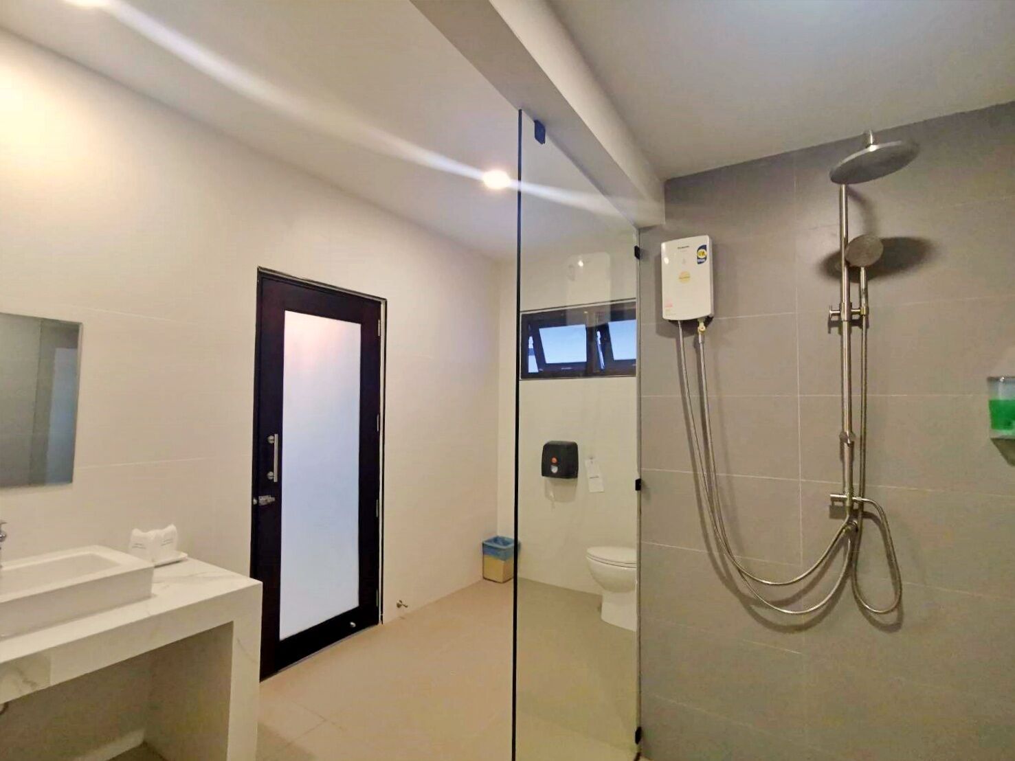 Un baño moderno con cabina de ducha de vidrio, un lavamanos blanco y una puerta que da a otra habitación.