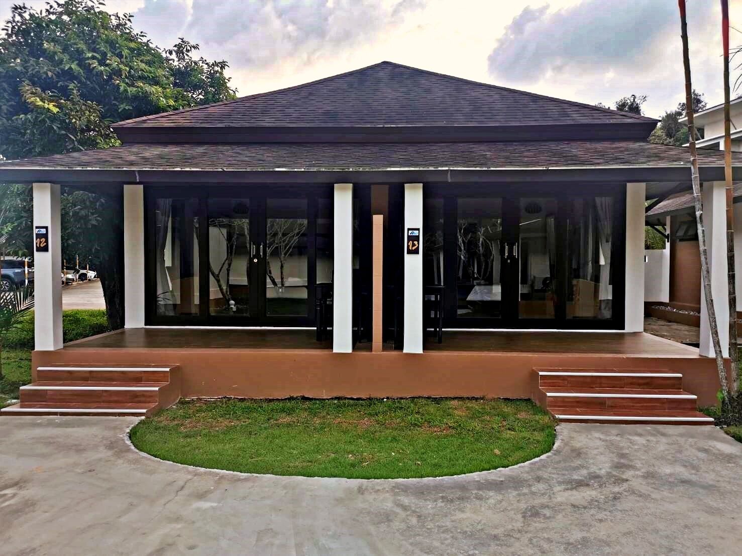 A modern building with a covered entrance, a grassy area in front, and a parking lot visible in the background.
