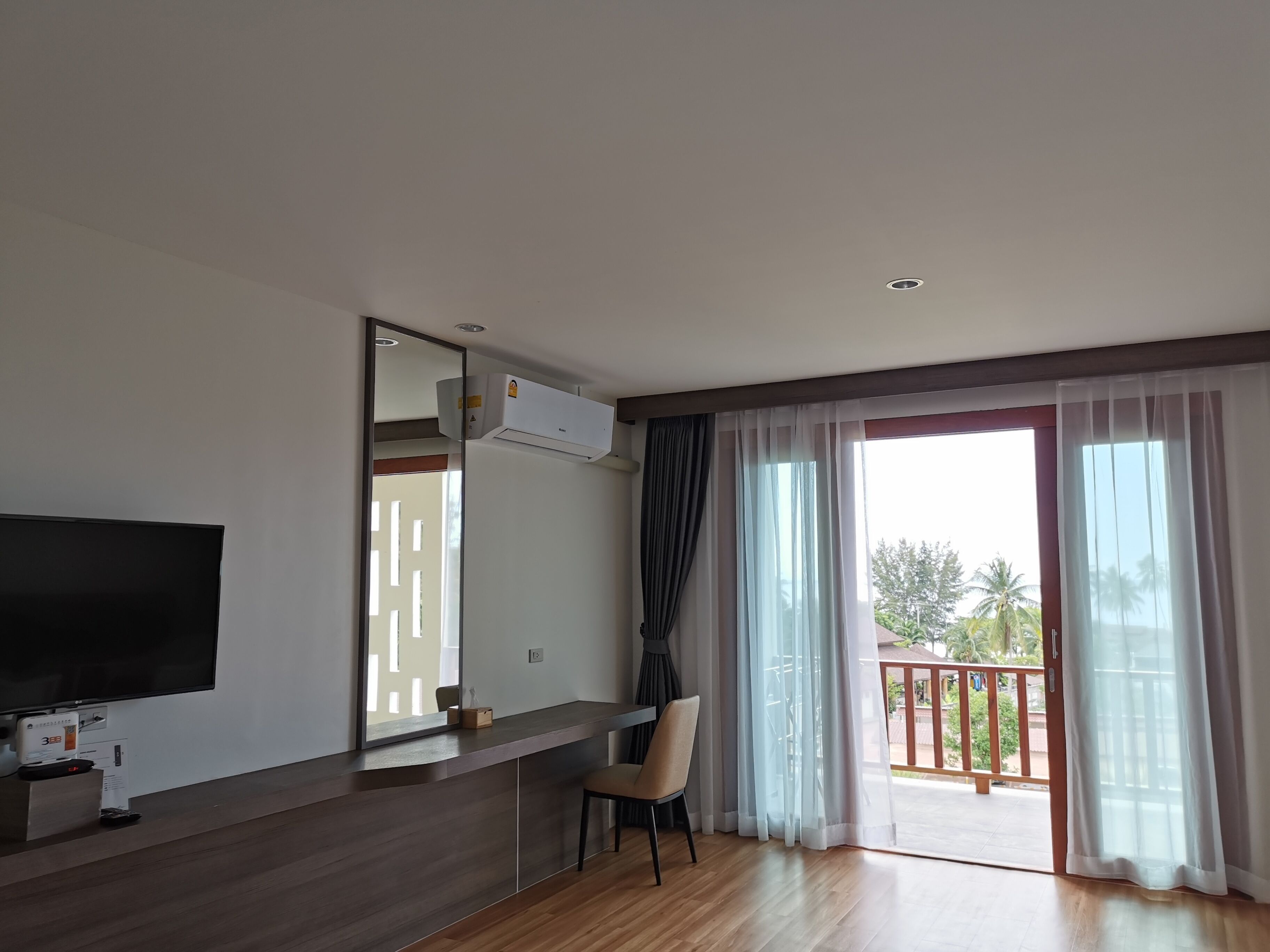 Una sala de estar moderna con una televisión de pantalla plana, una mesa de centro de madera, un sillón y un balcón con vistas a palmeras.