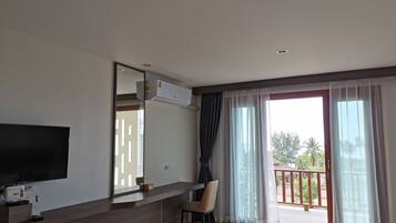 Una sala de estar moderna con una televisión de pantalla plana, una mesa de centro de madera, un sillón y un balcón con vistas a palmeras.