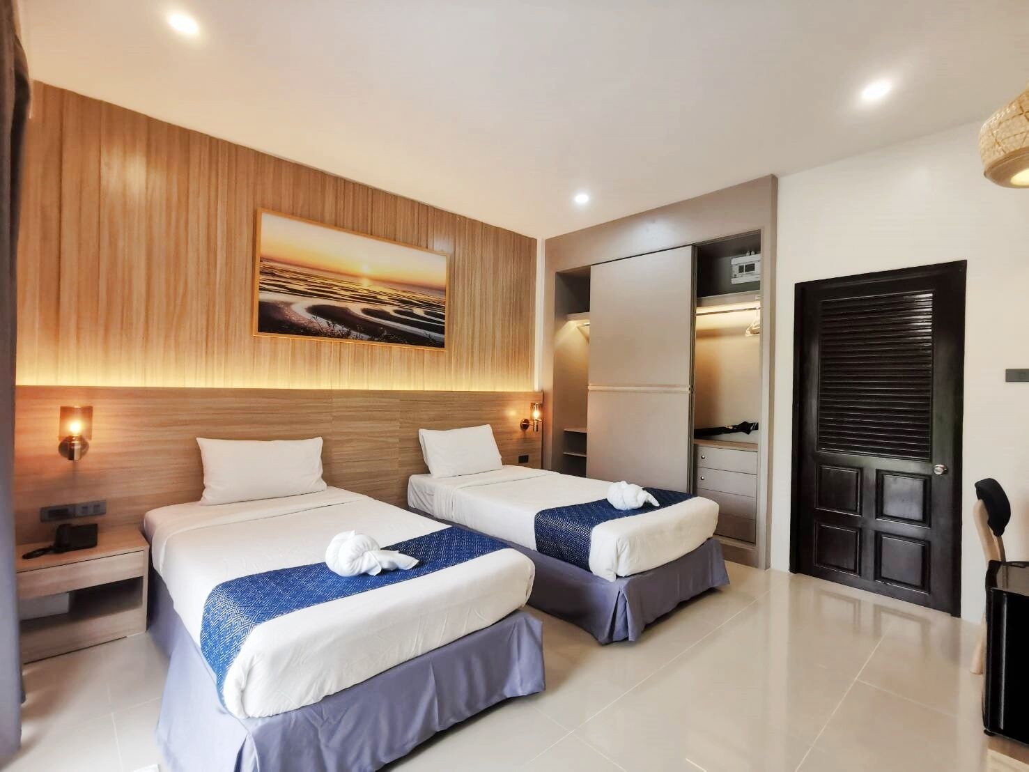 A modern hotel room with two beds, a large mirror, a wardrobe, and a painting on the wall.