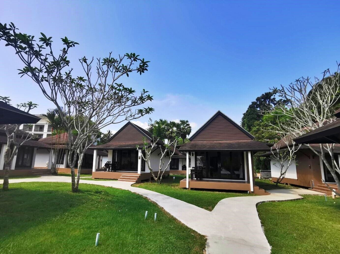 A row of modern, single-story buildings with flat roofs and covered verandas, surrounded by well-maintained grass and trees.