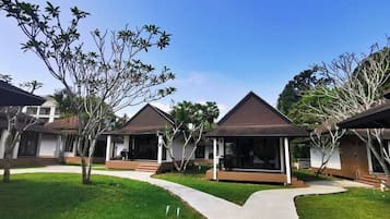 A row of modern, single-story buildings with flat roofs and covered verandas, surrounded by well-maintained grass and trees.