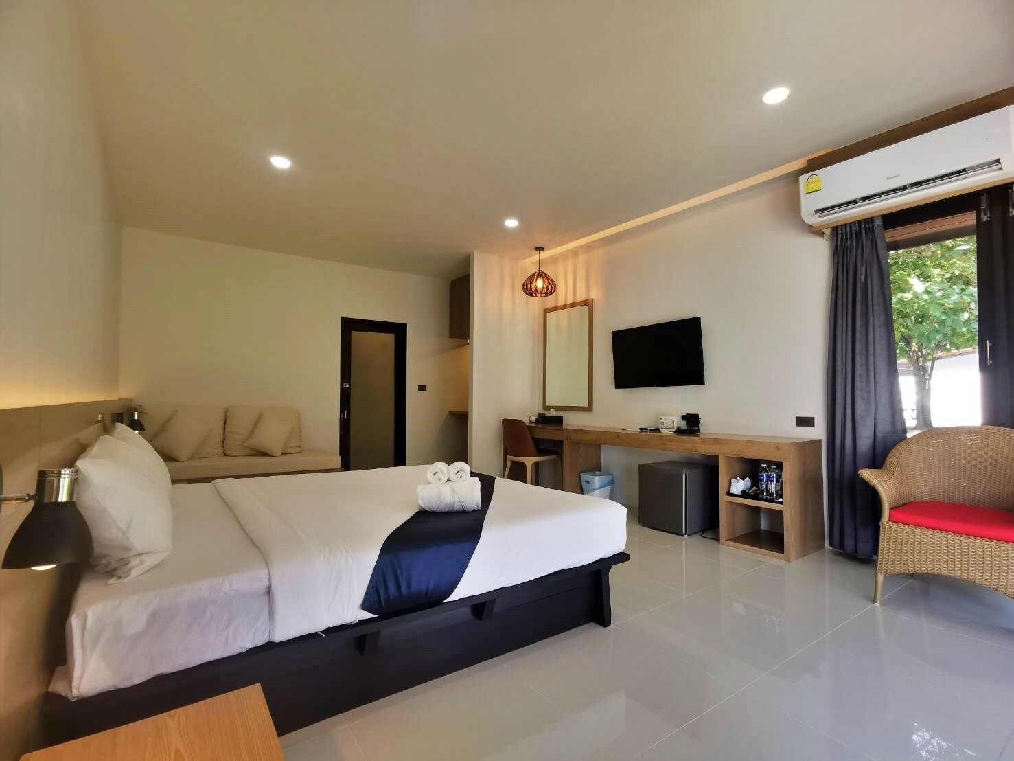 A hotel room with a bed, a desk, a chair, a television, and an air conditioning unit.