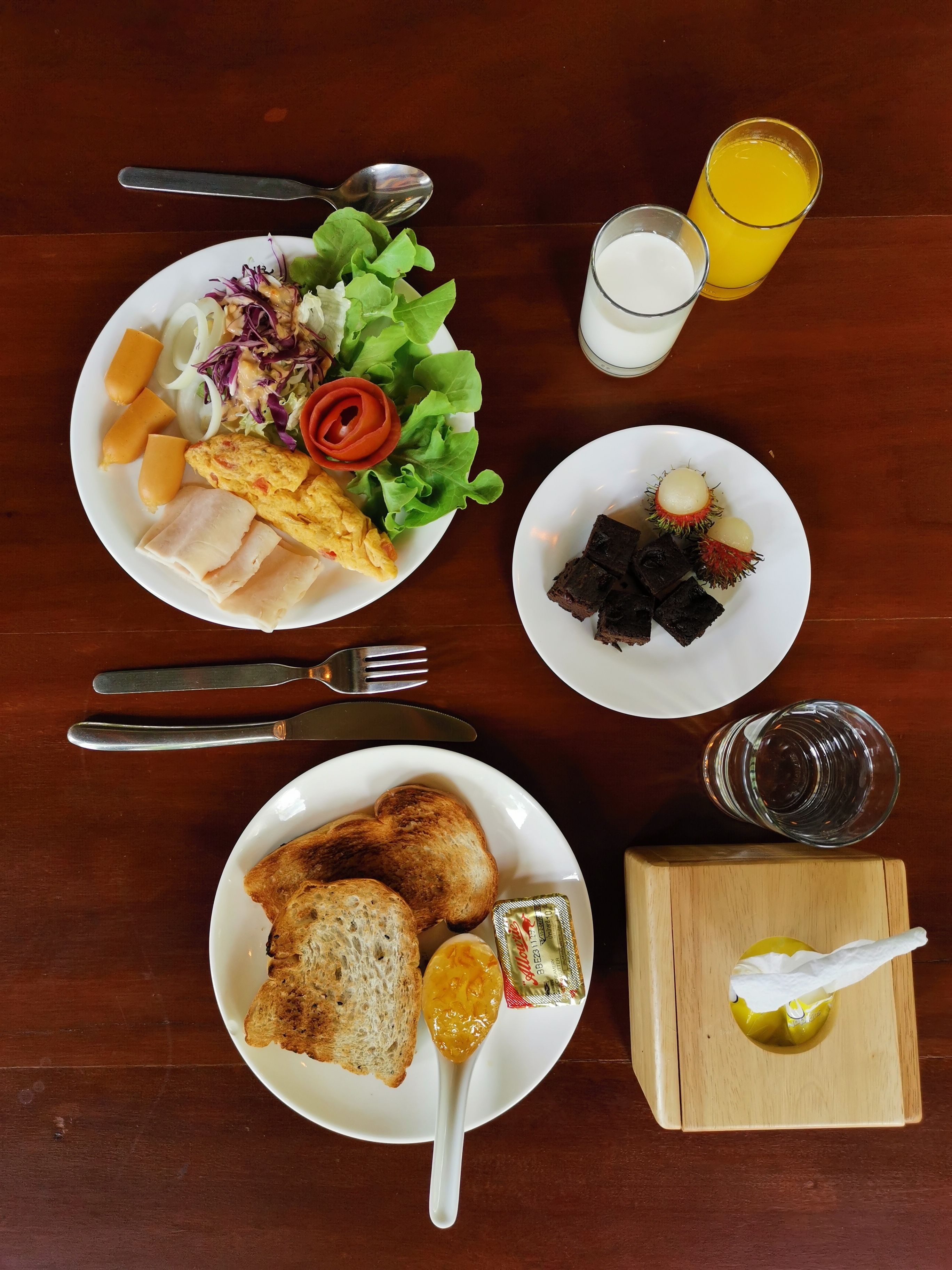 A table with plates of food, utensils, and a glass of orange juice.