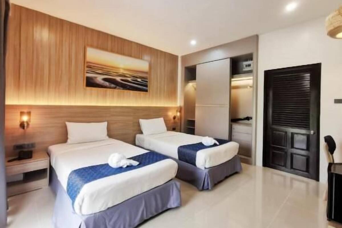 A hotel room with two beds, a wooden headboard, a painting, a wardrobe, and a door.